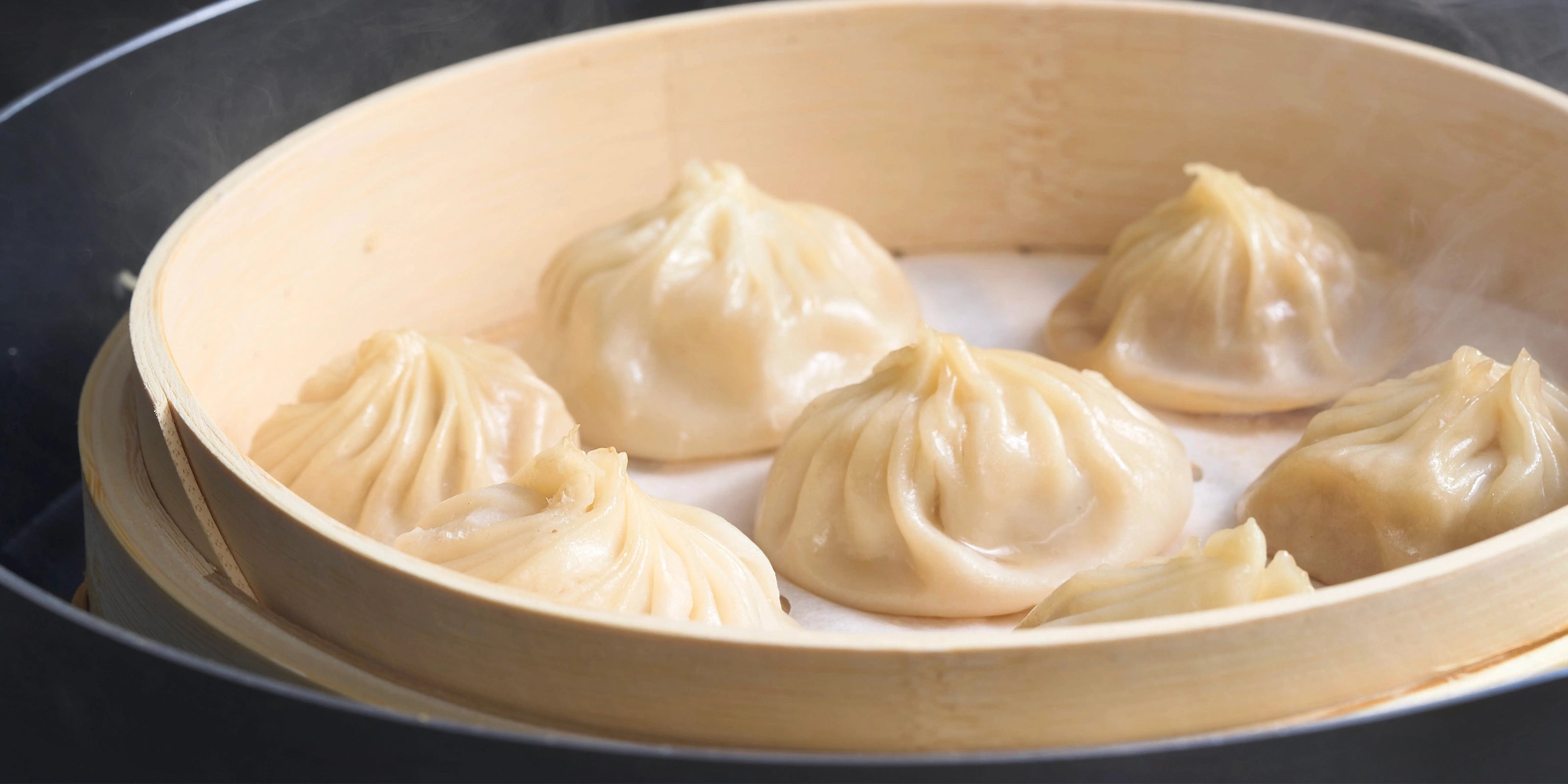 A close-up of thin-skinned soup dumplings in a steamer, highlighting the premium quality and consistency established by former 5-star hotel and Din Tai Fung chefs.